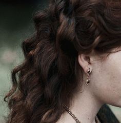 a close up of a woman with red hair wearing gold necklace and earring set