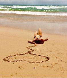 a woman laying on top of a sandy beach next to the ocean and writing in the sand