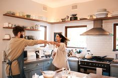 a man and woman in the kitchen pointing at each other's hand as they shake hands