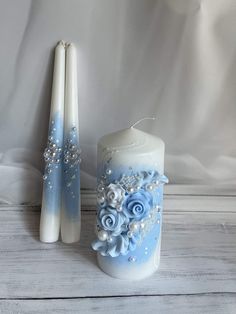 two candles are sitting next to each other on a white tablecloth with blue flowers and pearls