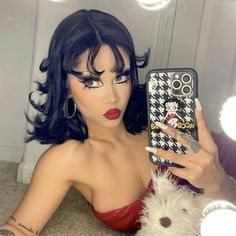 a woman with black hair and makeup holding a cell phone in front of her face