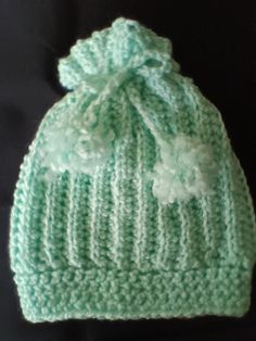 a green knitted hat with white flowers on the front and side, sitting on a black surface