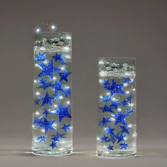 two clear vases with blue stars in them on a gray background, one is lit up and the other has lights