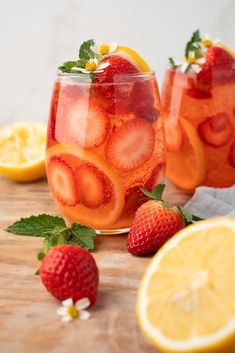 two glasses filled with lemonade and strawberries next to sliced lemons on a cutting board