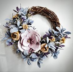 a wreath with purple flowers and greenery on it sitting on a white surface in front of a wall