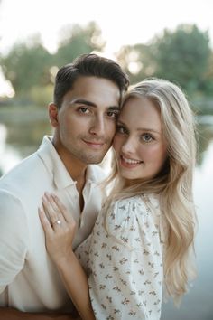 a man and woman standing next to each other in front of a body of water