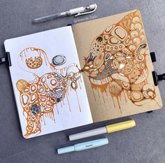 an open notebook with drawings on it next to a pen and two other items in the background