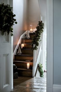 candles are lit on the steps leading up to an entryway with wreaths and greenery