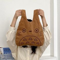 a woman holding up a totoro bag over her head