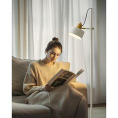 a woman sitting on a couch reading a book in front of a lamp that is next to her