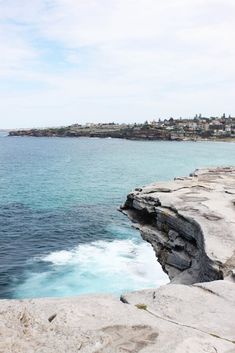 the water is blue and choppy with waves coming in from the rocks on the shore