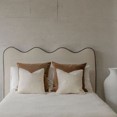 a white bed with two pillows on top of it and a vase next to it