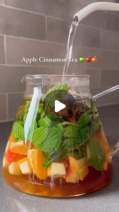 an apple cinnamon tea is in a glass pitcher with strawberries and mint leaves on top