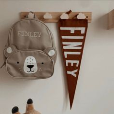 a teddy bear backpack hanging on the wall next to a wooden sign that says finley