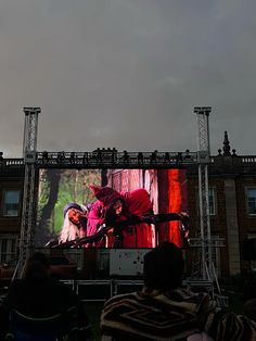 people watching a large screen on the side of a building