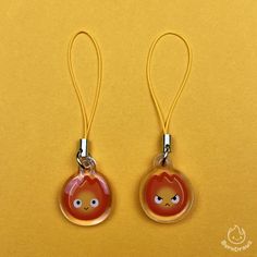 two red earrings with faces on them are hanging from yellow cord against a yellow background