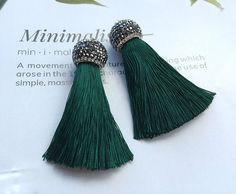 the green tassel earrings are on top of a piece of paper with silver beads