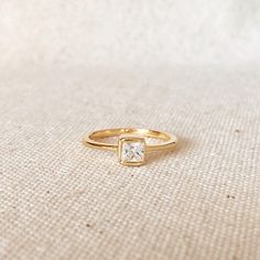 18k Gold Filled Stack-able Square Solitaire Ring features a 1.5 mm wide band with a single 5mm Square bezel Cubic Zircon Stone. Perfect to stack with other rings. * Metal: 18k Gold Filled * Available in sizes 5, 6, 7, and 8 * Weight: 1.8 grams * Band: 1.5mm wide * Stone: 5mm * Hypoallergenic jewelry * Handcrafted in Brazil Learn how to care for your jewelry with these easy instructions. Properly handling and caring for your ArtBossa jewelry is essential in maintaining its pristine condition. 1. 14k Gold Stackable Princess Cut Rings For Gift, Gold Princess Cut Solitaire Birthstone Ring, Minimalist Gold Princess Cut Rings, Gold Princess Cut Birthstone Ring, Princess Cut Stackable Rings As Gifts, Rings Metal, Pearl Love, Square Stone, Hypoallergenic Jewelry