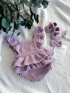 a crocheted baby outfit and booties on a bed next to a plant