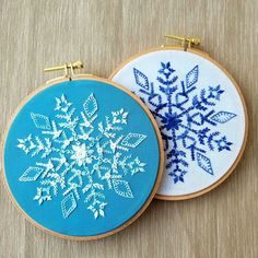 two hand embroidered snowflakes sitting next to each other on top of a table