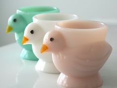 three ceramic birds are sitting next to each other on a white counter top, one is pink and the other is green