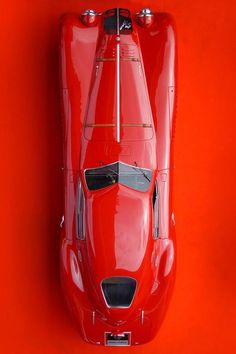 an overhead view of a red sports car on a bright orange background with the hood down