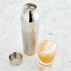 a drink in a glass next to a metal shaker on a marble counter top