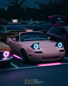 two cars parked in a parking lot with their headlights turned on and the front lights glowing pink