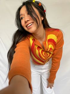 cropped orange cardigan with red, orange, and yellow heart design available in sizes xs, s, m, l model is 5'3" and wearing a size small Yellow Cropped Cardigan Outfit, Retro Orange Cardigan For Winter, Orange Crochet Cardigan, Red Crop Cardigan, Retro Orange Spring Cardigan, Orange Cardigan, Yellow Heart, Heart Design, Shirts Tops