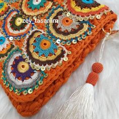 an orange crocheted purse with tassels and beads on the front, sitting on a white furnishing