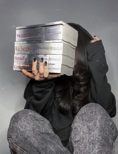 a woman is sitting on the floor holding two books in front of her head and covering her face with both hands