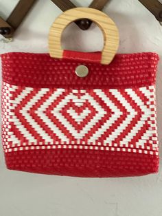 a red and white woven bag hanging from a hook on a wooden rack with hooks