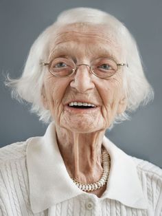 an older woman with glasses and a white sweater smiling at the camera while wearing a pearl necklace