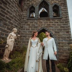 two people standing next to each other in front of a stone building with statues on either side