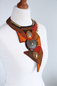 Extra large African necklace for women and man, for all genders. Statement necklace was created in three main colors: brown, red an orange. Tribal necklace is combined from a geometric forms. It has two main man made stones and metal buckle in the middle. The stones and buckle in each order can be slightly different. It is made to order art piece, it will be create just for you. Necklace collar is adjustable with lobster claw on the back. Made of: Metal buckle. Brown, red, orange and black seed Unique Embellished Festival Jewelry, Beaded Pendants, Collar Necklaces, Beaded Collar Necklace, Festival Earrings, Long Statement Necklace, Spike Necklace, African Necklace, Bold Necklace