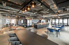 an office with tables, chairs and bar area in the middle of the room is lit by pendant lights