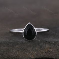 a white gold ring with a black tear shaped stone in the center on a rock