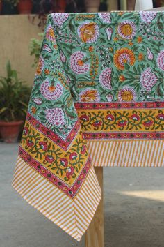 an image of a table cloth on top of a wooden stand with potted plants in the background