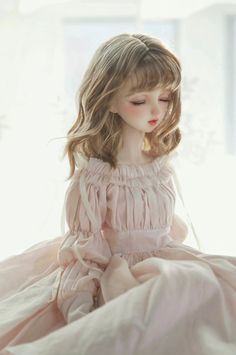 a doll sitting on top of a bed wearing a pink dress with ruffles