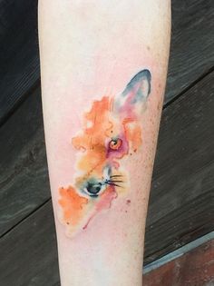 a watercolor fox tattoo on the left calf's leg, with orange and pink colors