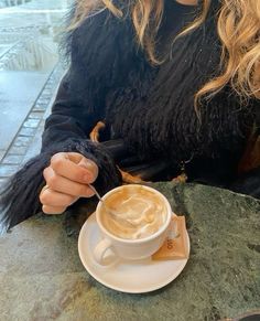 a woman sitting at a table with a cappuccino in her hand,