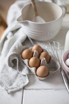 some eggs are in a carton on the counter next to a whisk