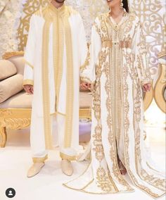 two people standing next to each other in white and gold outfits