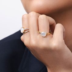 a close up of a person wearing a gold ring with a white stone on it