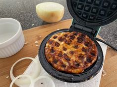 an open waffle iron sitting on top of a wooden table next to onion rings