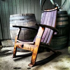 a wooden rocking chair sitting next to two wine barrels and a barrel on the ground