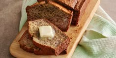 sliced loaf of banana bread with butter on wooden cutting board next to green dish towel