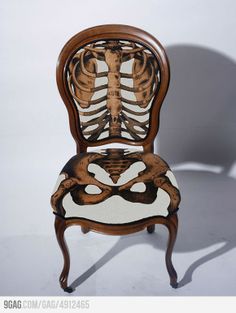 a skeleton sitting on top of a wooden chair next to a white wall and floor