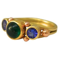 Experience the allure of our handcrafted Cabochon Colombian Emerald Sapphire Ring, an exquisite work of art by Lynn Kathyrn Miller, a renowned artisan at Lynn K Designs. This ravishing piece of fine jewelry is a testament to our dedication to quality craftsmanship, designed to captivate and leave an unforgettable impression. Set in the ethereal beauty of 18k Royal Yellow Gold, this ring is a timeless masterpiece, highlighting a mesmerizing cabochon-cut Colombian Emerald. The verdant hue of the e Royal Yellow, Alexandrite Ring, Gold Rings Jewelry, Colombian Emeralds, Handcrafted Artisan Jewelry, 18k Gold Jewelry, Periwinkle Blue, Ethereal Beauty, Unique Earrings