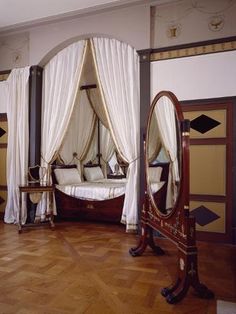 an ornate canopy bed sitting in a bedroom next to a mirror and wooden flooring